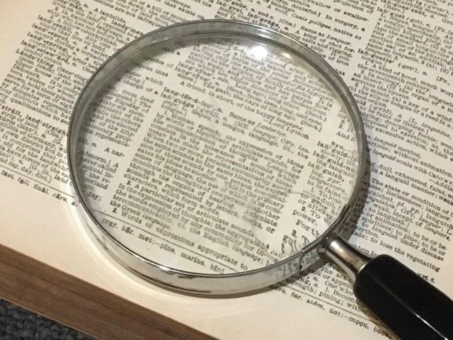 A large magnified glass sits on top of a paragraph of words in a book.