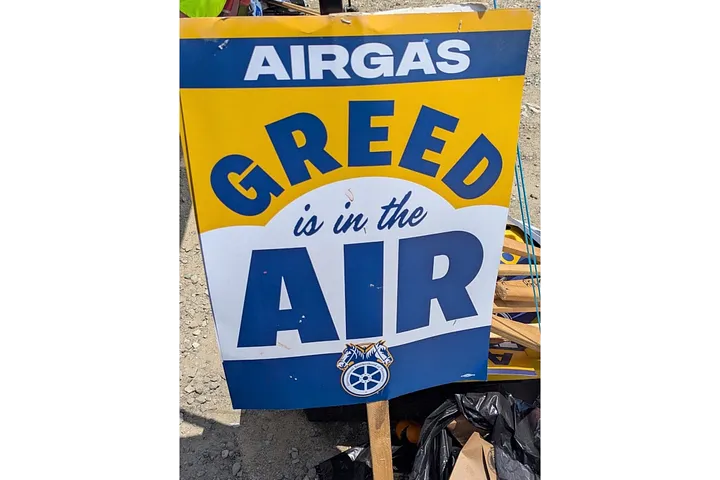 Picket sign reading “Airgas Greed is in the Air” stands on the ground.