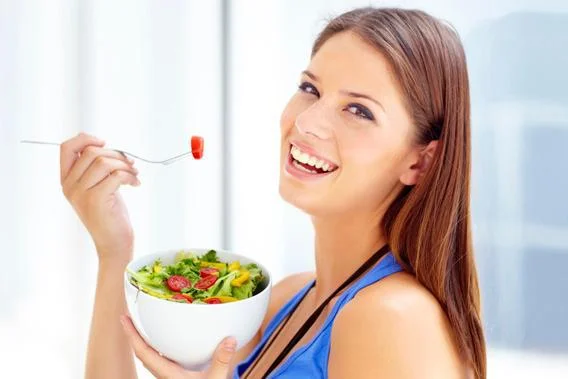A woman with no light in her eyes smiling while eating a salad