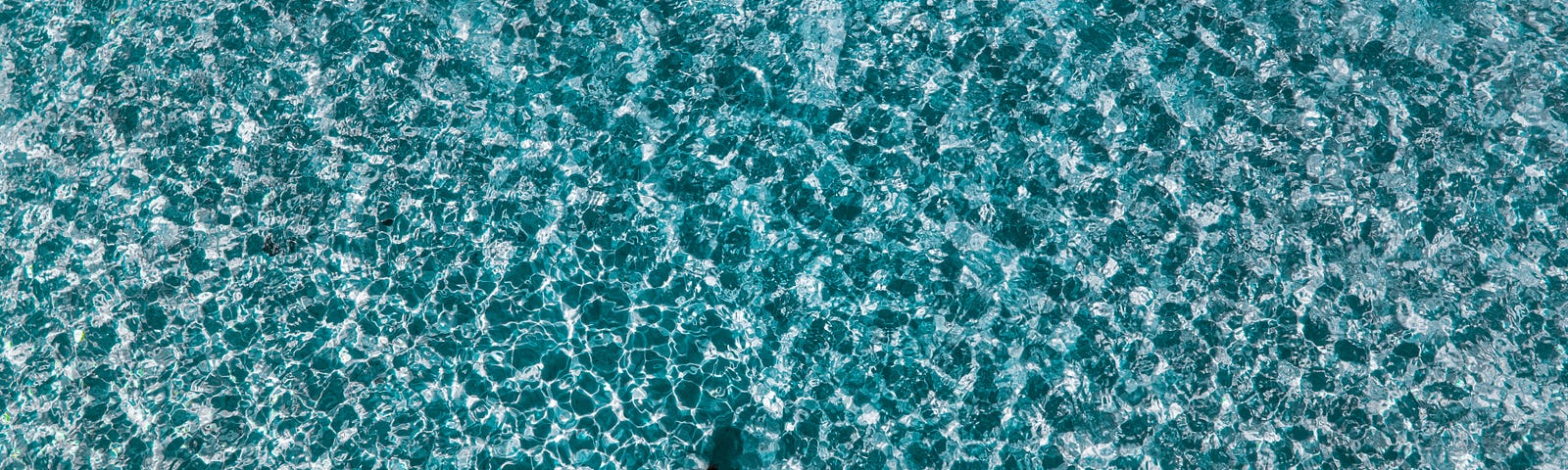 Woman in a bikini floating in the middle of a turquoise sea that looks like a mosaic.
