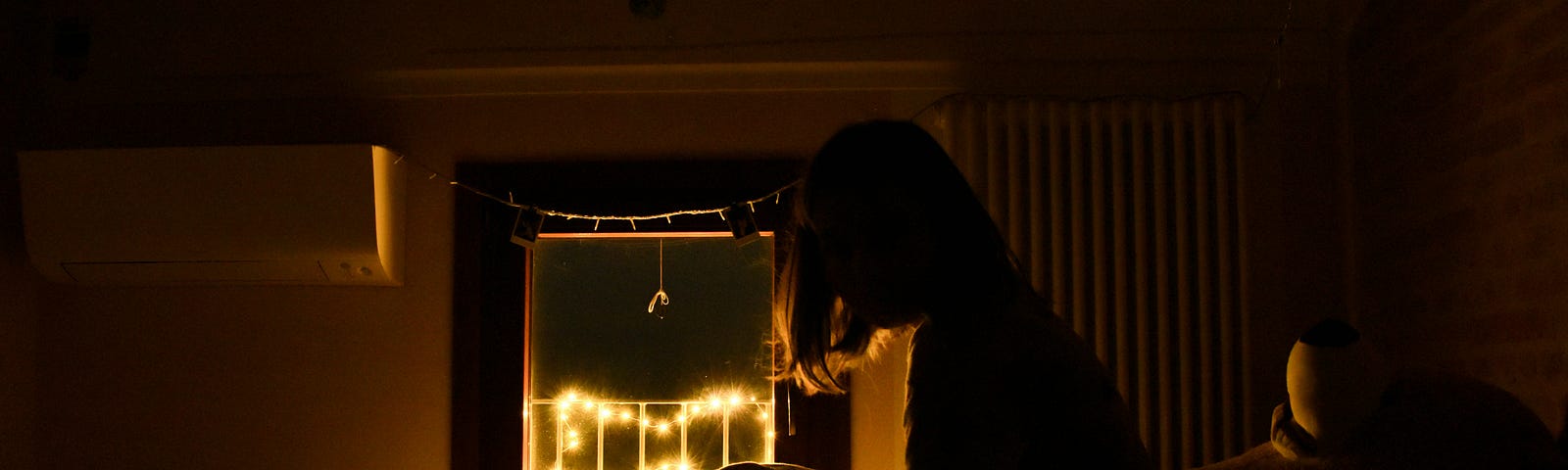 woman sitting up in bed in dark room with christmas lights outside