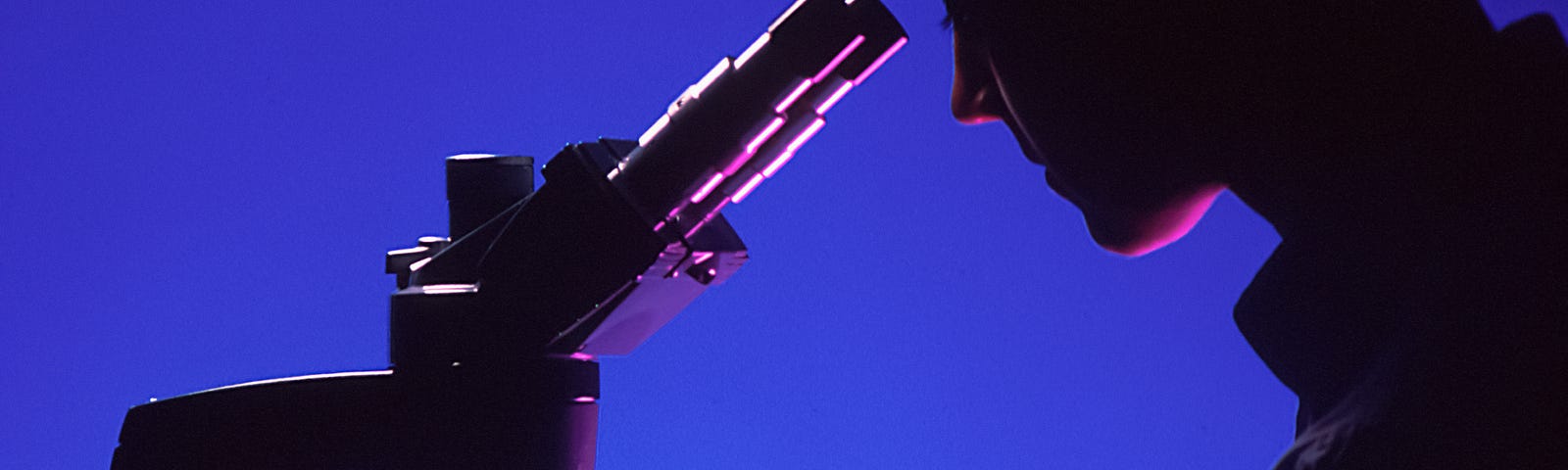 Shadow image on blue background of person in profile peering through microscope.
