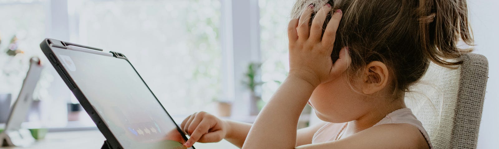 A little girl using a digital tablet in a worried position on the table.