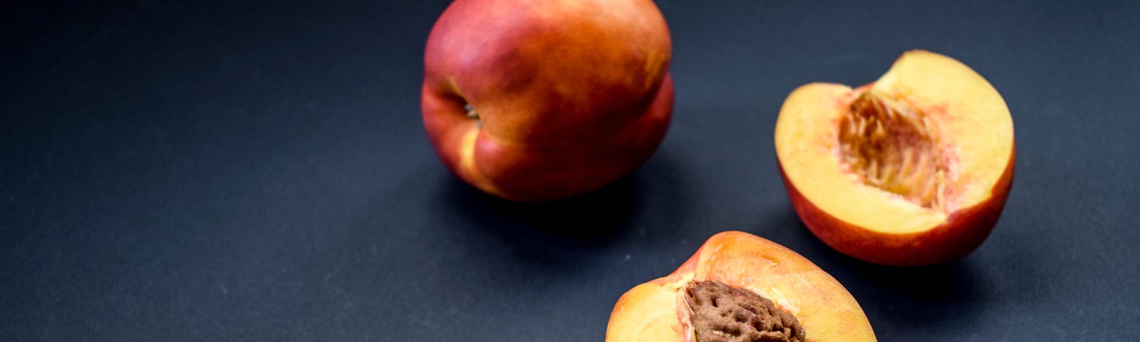 Image of a whole peach and a fresh peach cut in half with pit still visible in other half.