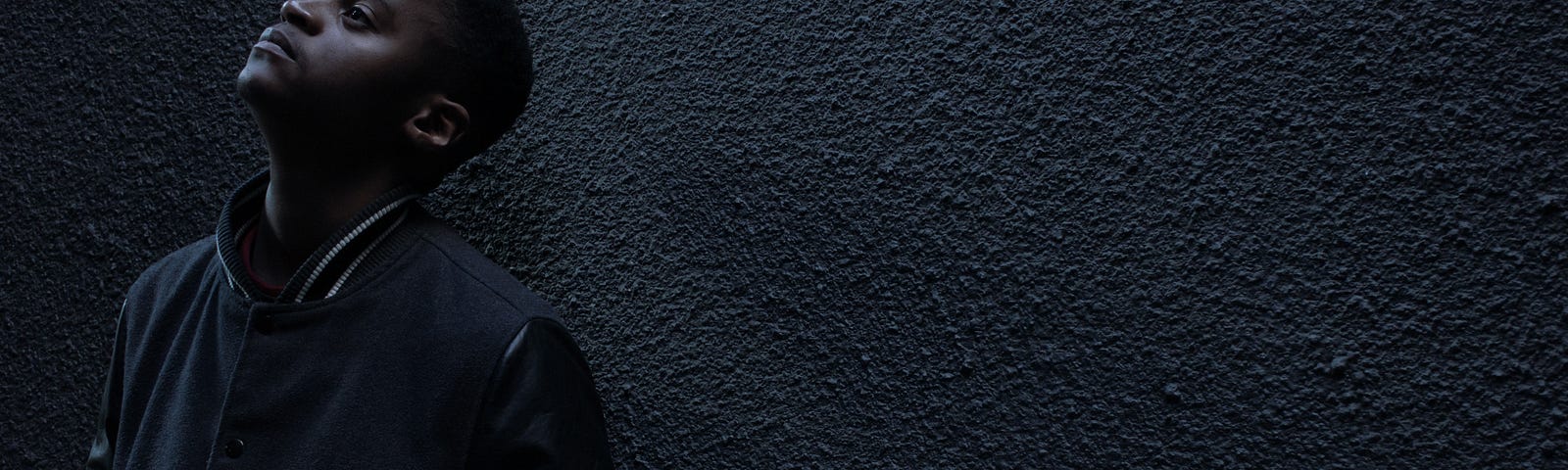 A young man leaning against a stone wall waiting for something or someone.