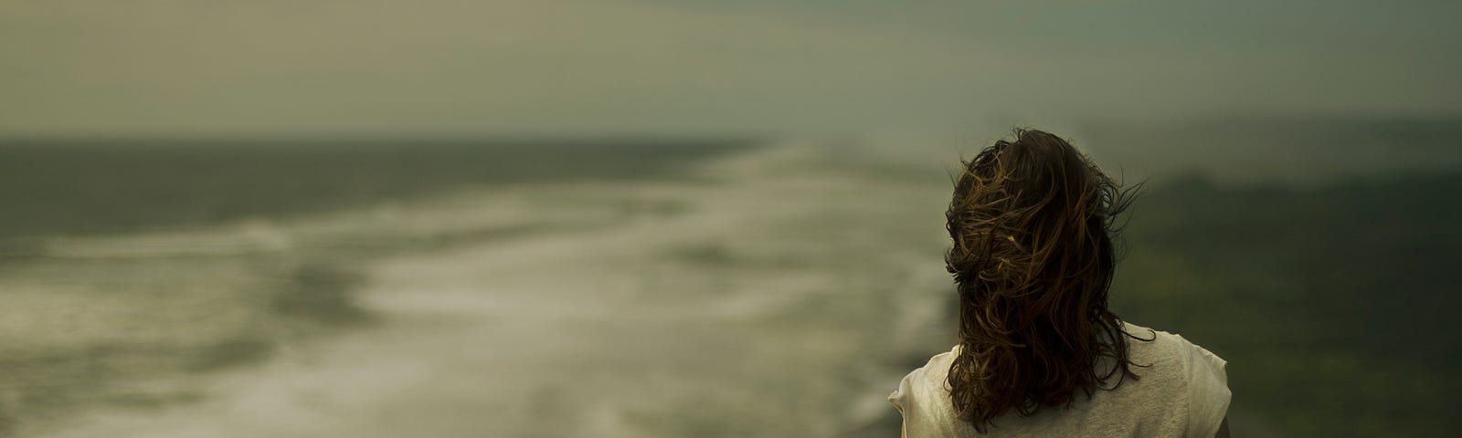 A woman walks away from us on a beach, the ocean waves to her left. The photo has a depressive, mutted color palette. We may someday use blood tests — such as serum LDH — to identify suicide risk among those with a major depressive disorder.