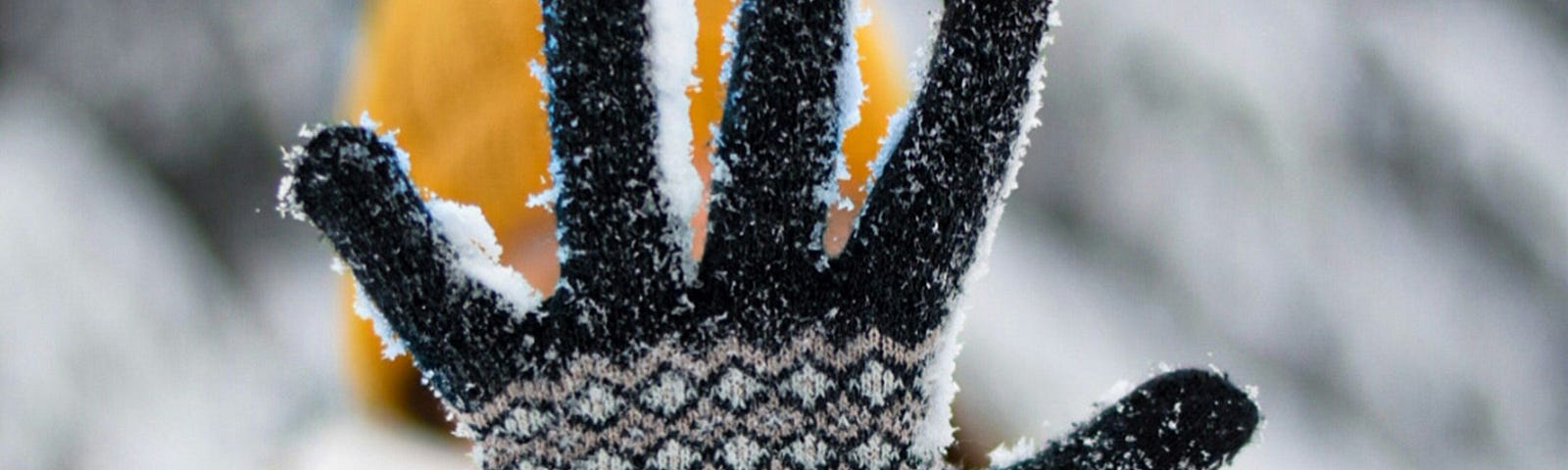 A woman with a yellow hat and an outstretched arm. She’s wearing a black and white glove. The background is a blurred winter scene.