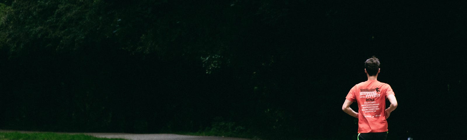 A man in a red shirt and black shorts running on a paved, winding path alongside a body of water