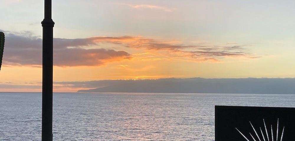 Sunset over La Gomera, one of the Canary Islands, the light is tropical hot orange and yellow with a little cloud, against a pale blue sky, the island is seen from Tenerife, around 40 km away, so the sea between reflects the light