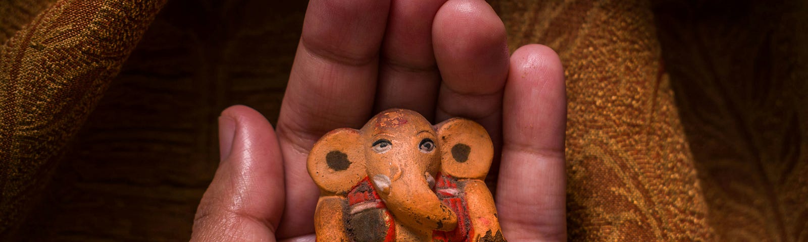 a hand holding a small statue of Ganesh, an elephant god