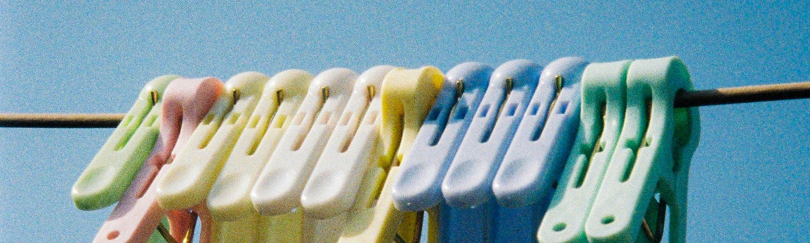 A close-up of a bunch of pastel-colored laundry clips on a clothesline against a bright blue sky.