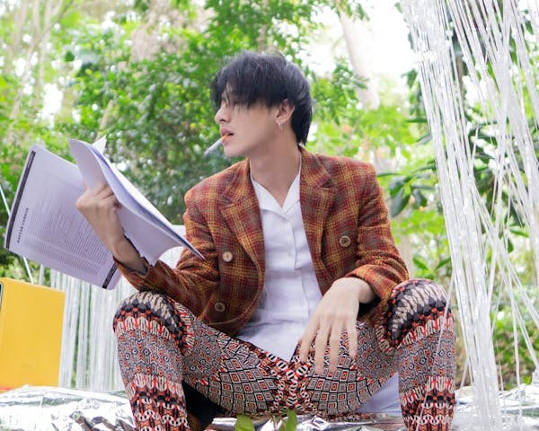 Stylish man reading a printed article while sitting on foil steps in his garden and smoking a cigarette