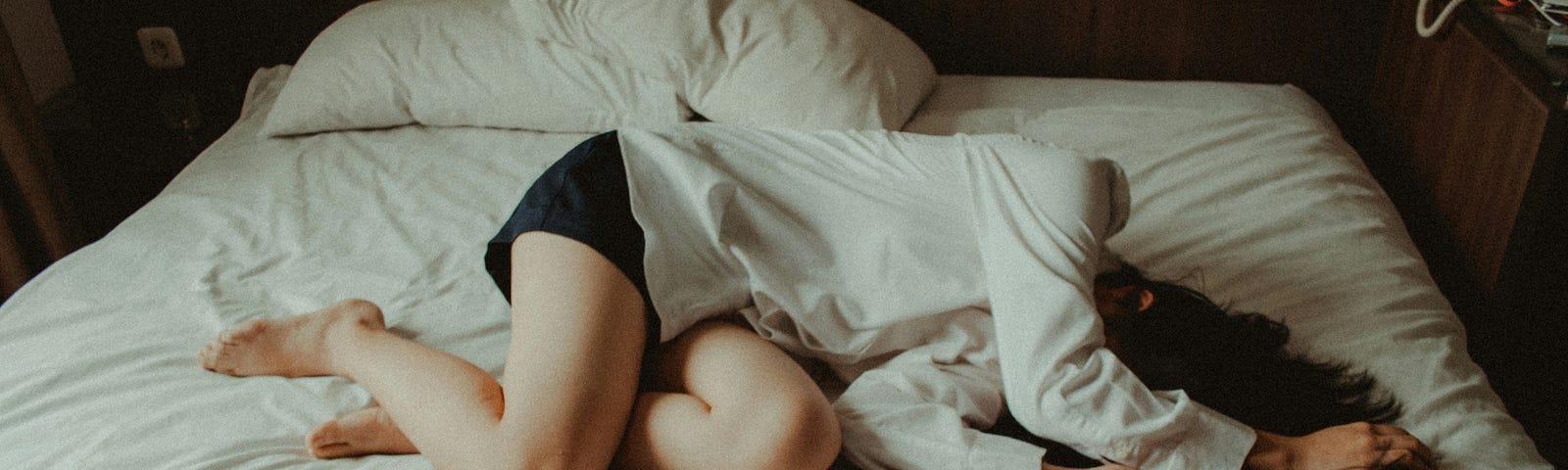 Girl curled up on an unmade bed with her arms over her face.