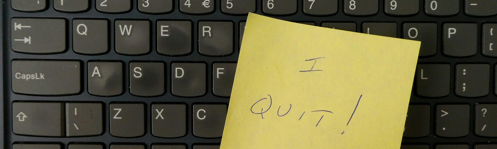 Computer keyboard with a post-it note and the words, “I Quit” written on the note.