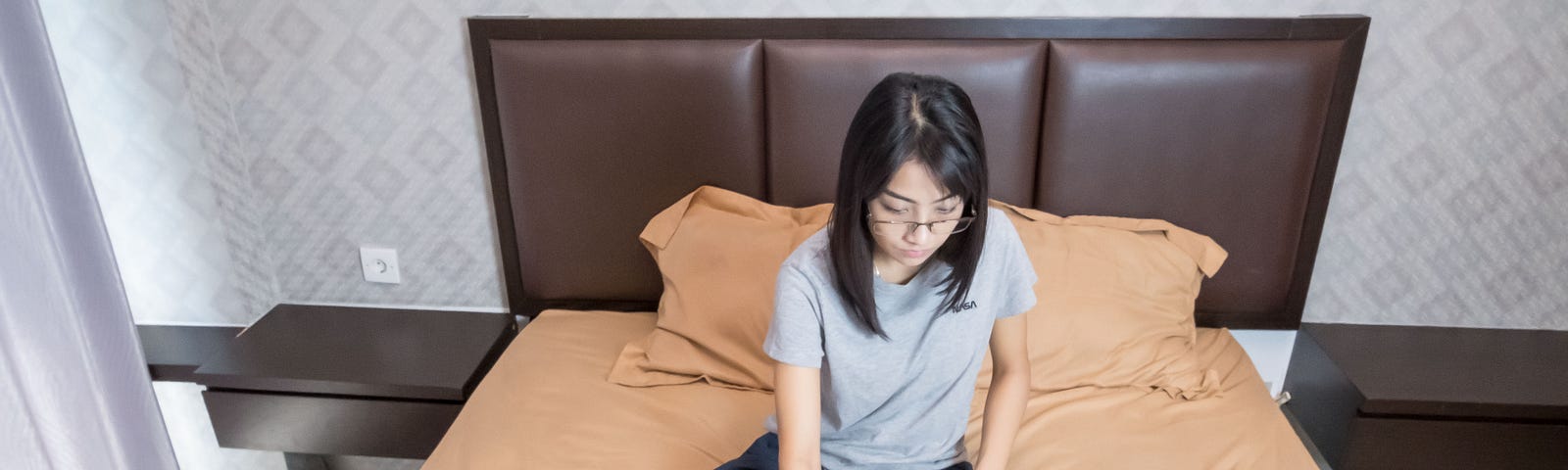 Woman sitting on bed with books and typing on laptop.