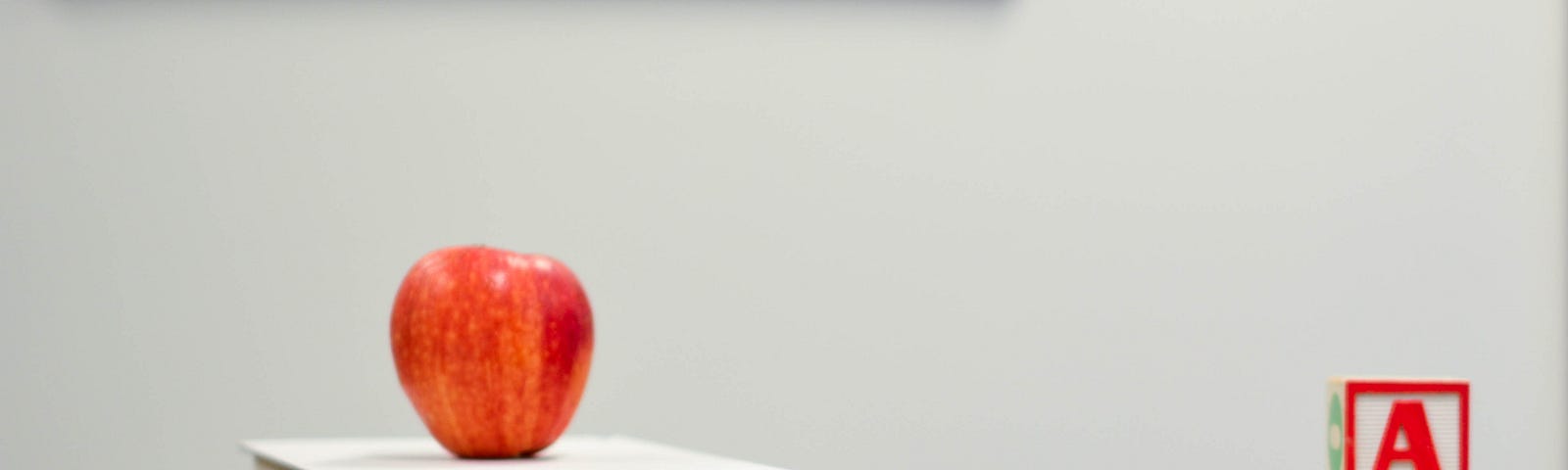 An apple placed on a pile of books. Pencils and cubes in the form of the alphabet characters are placed on the table.