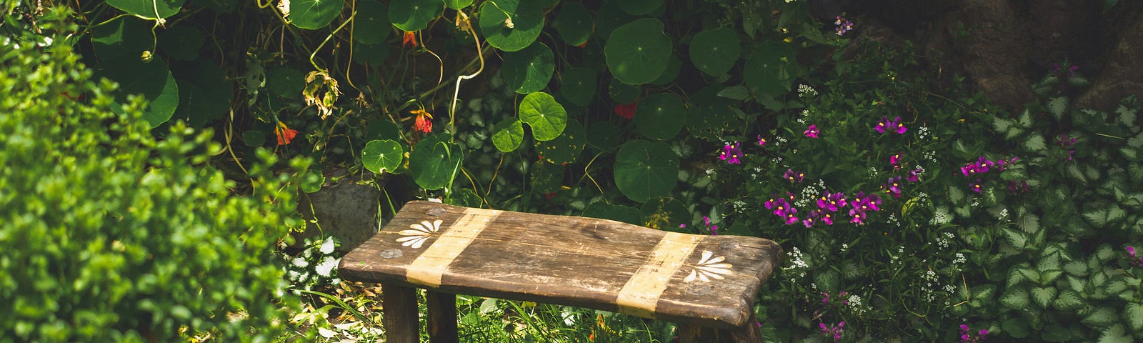 A small brown wooden bench/stool in a lush green garden with small flowers in the background.