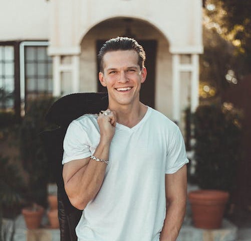 Man in white v-neck t-shirt and black pants smiling at the camera looking relaxed