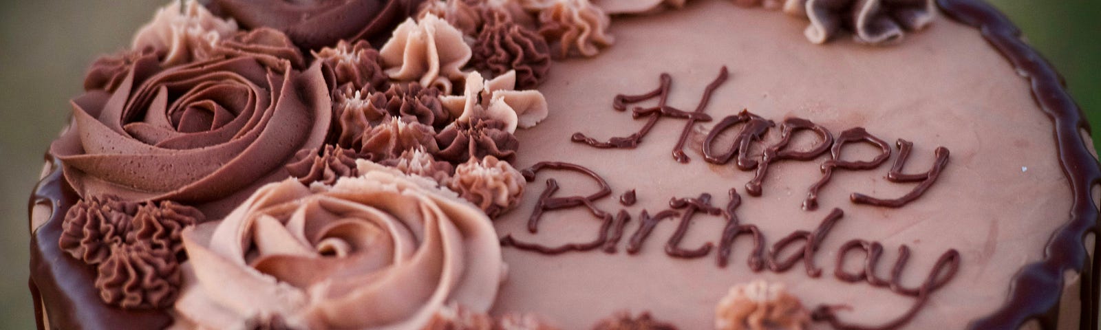 A chocolate frosted cake with rosettes saying “happy birthday”