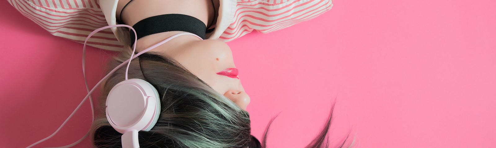 upside down picture of a woman with headphones and her hair hiding her eyes in a pink background