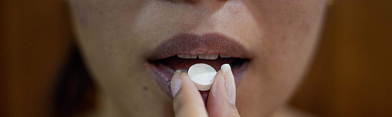 A woman faces us as she uses her left hand to bring a white pill towards her mouth.