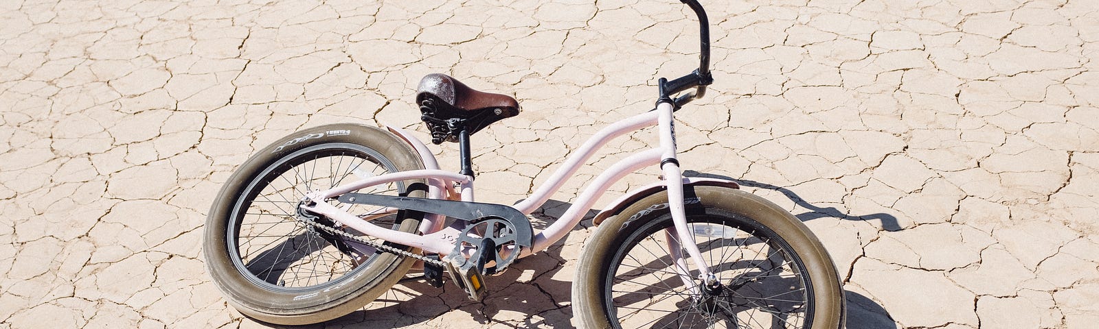 A dusty child’s bicycle abandoned in a dry, cracked riverbed.