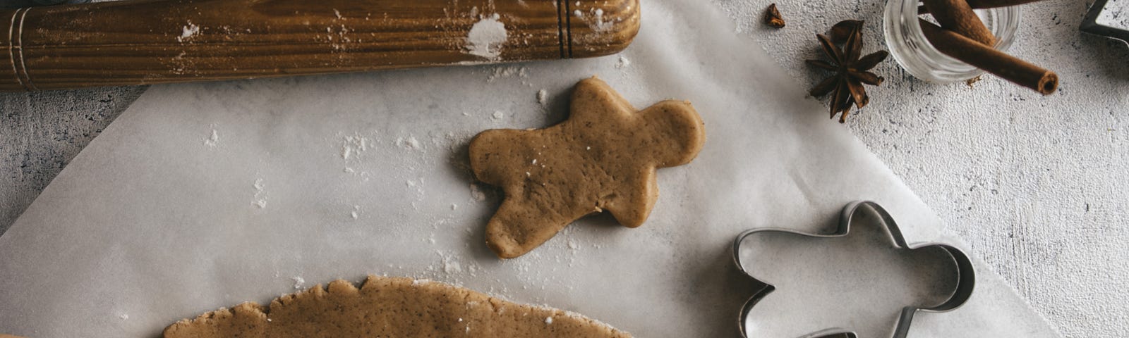 A child’s hands are pictured using a cookie cutter to cut gingerbread men from dough.