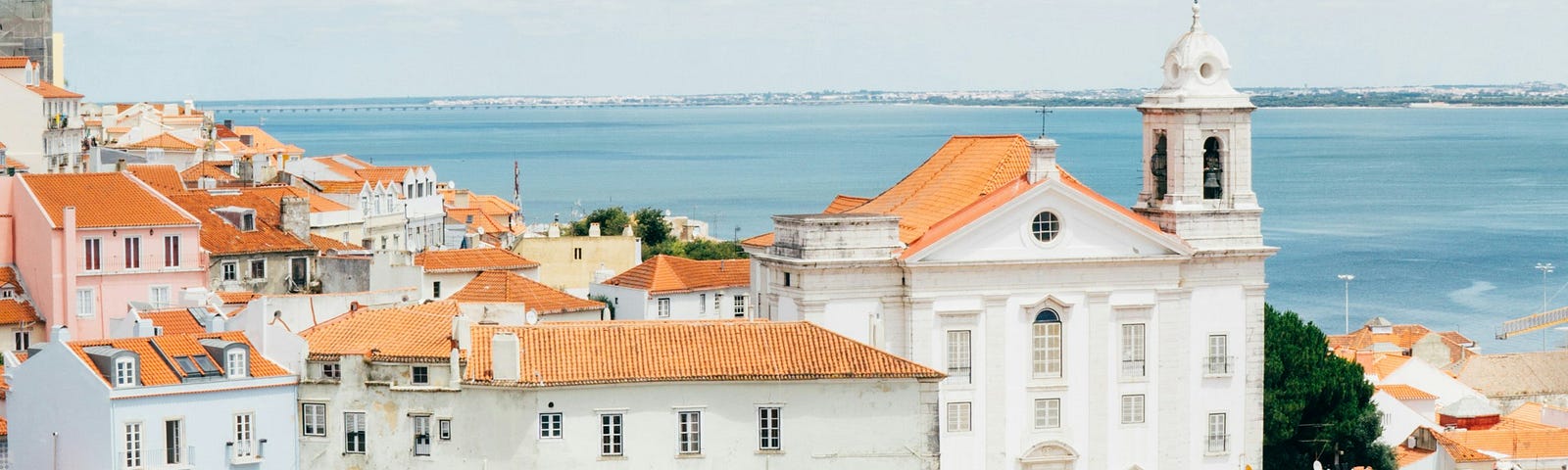 The beauty of Portugal on the coast with red roofed buildings, water in the background, and sun shining bright.