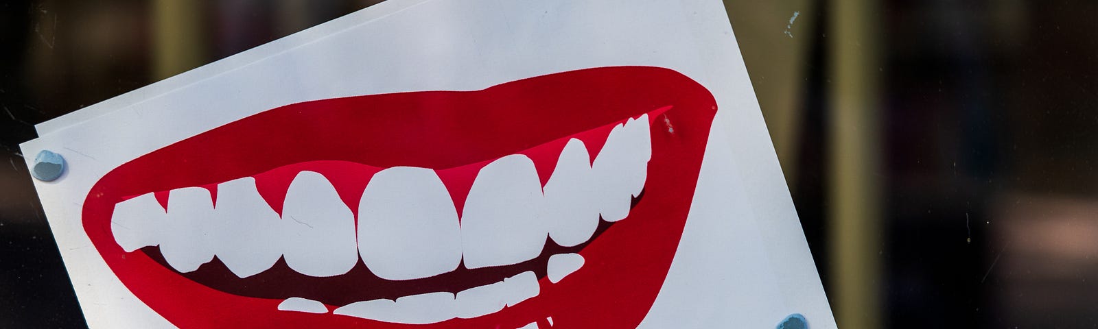 Cartoonish drawing of bright red lips with giant white teeth on white card