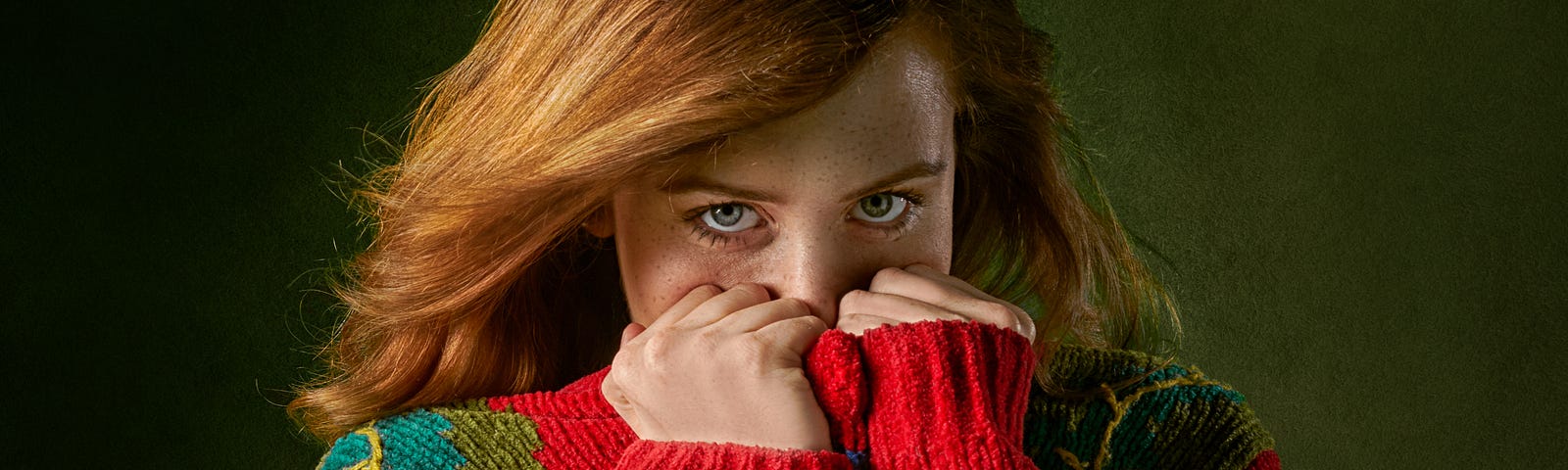 A shy redheaded woman hiding the lower part of her face in her sweater.