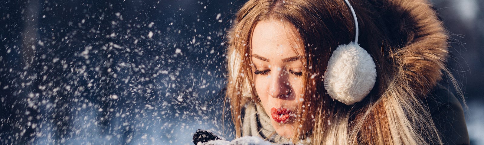 A woman in a coat, blowing a handful of snow into the air