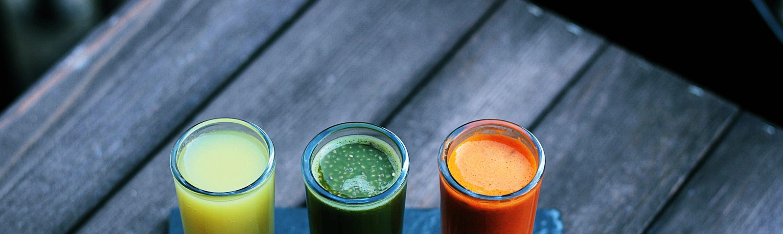 three glasses with healthy protein drinks, one yellow, one green and one orange