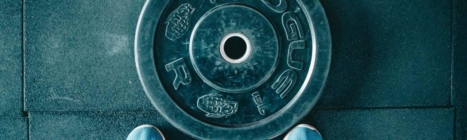 We see a weightlifting plate, with the lower legs and training shoes of an individual. The photo is from above.