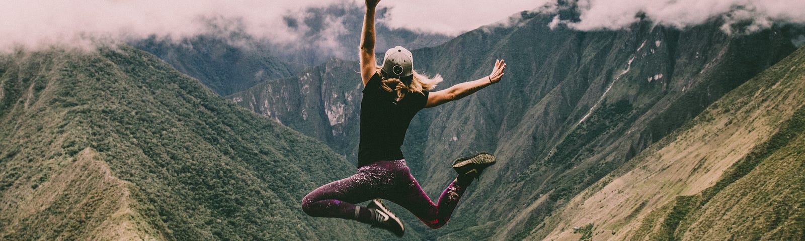 someone is jumping exuberantly, with a dramatic green valley and mountain in the background.