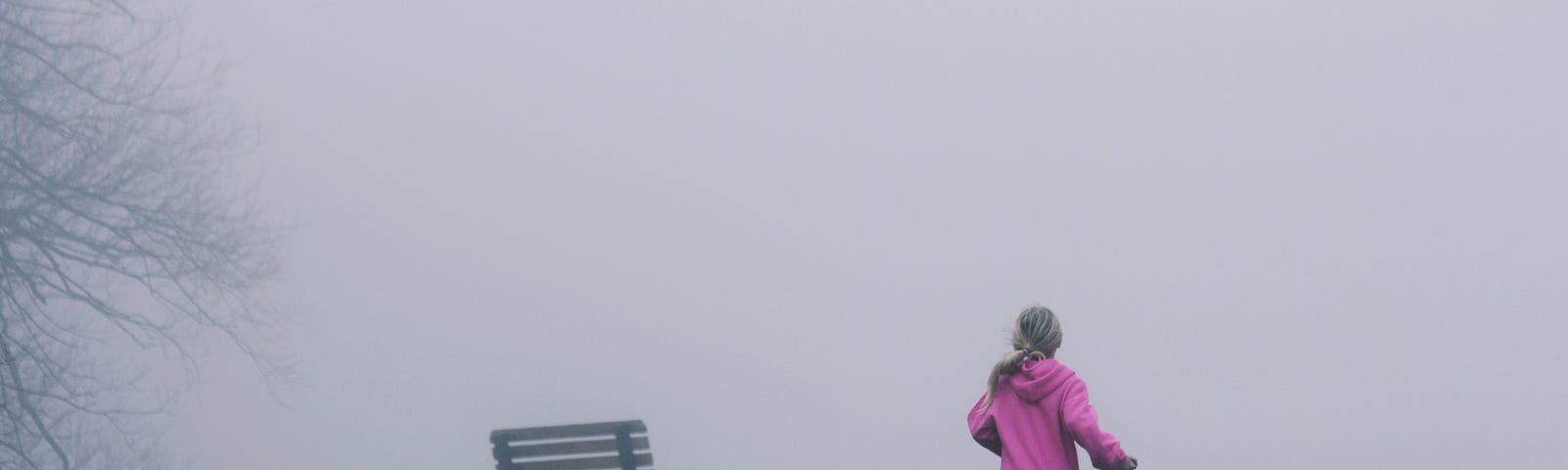 A young girl running away across a grassy area in fog