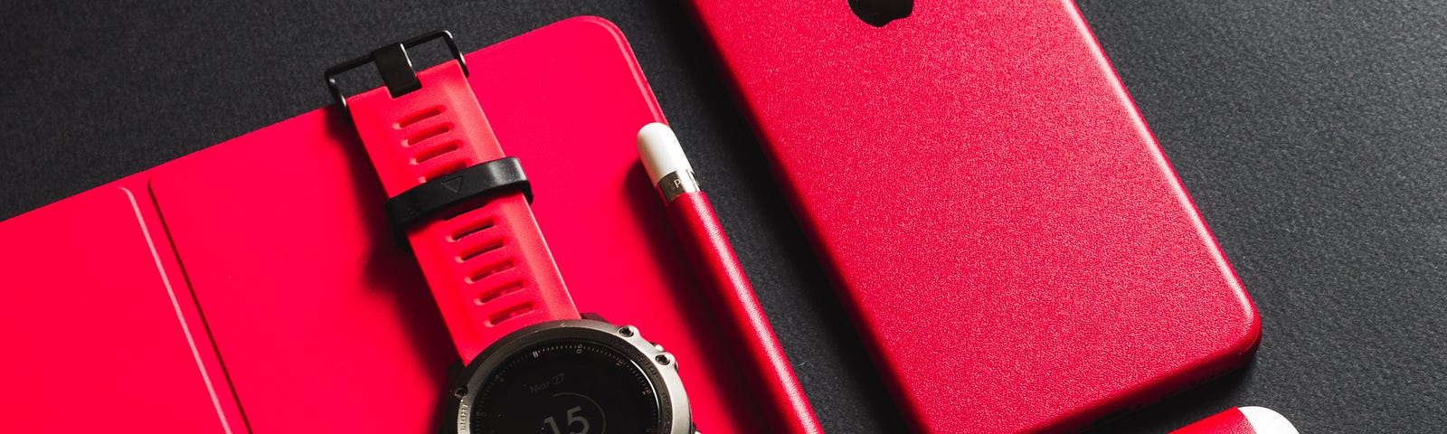 An all red, black and white set of different wearable techs such as Air Pods and a Smart Watch.