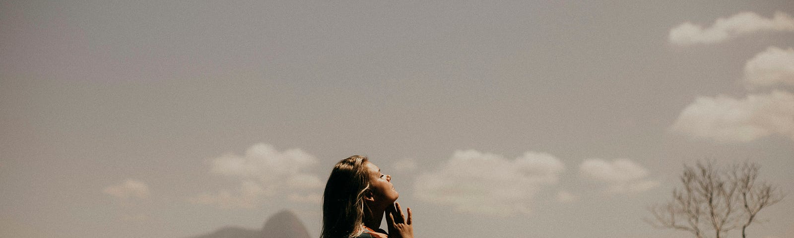 woman standing outside, facing the sky and mountains
