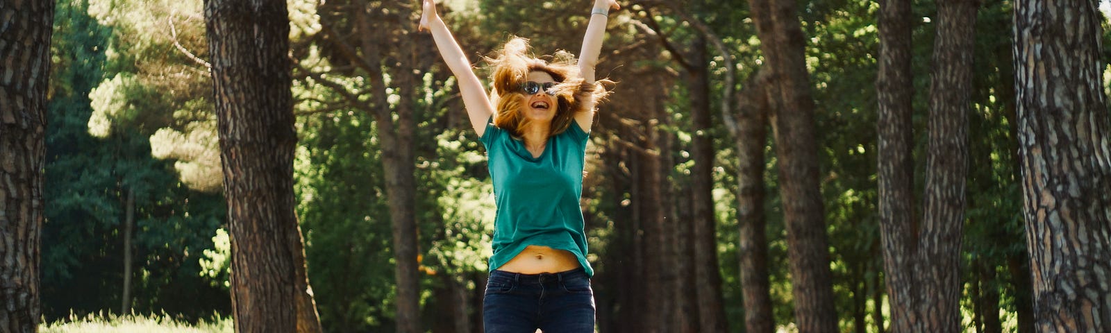 woman on a walking path jumping in the air with knees bent and hands in the air