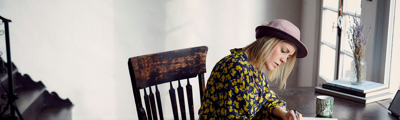 pretty blonde woman writing on a piece of paper while sitting on an old wooden chair