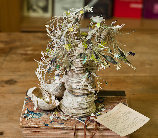 a tree that is crafted out of the pages of a book, shown in a photograph on top of an older book