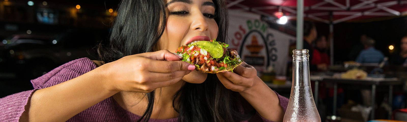 A young lady eating an overfilled taco