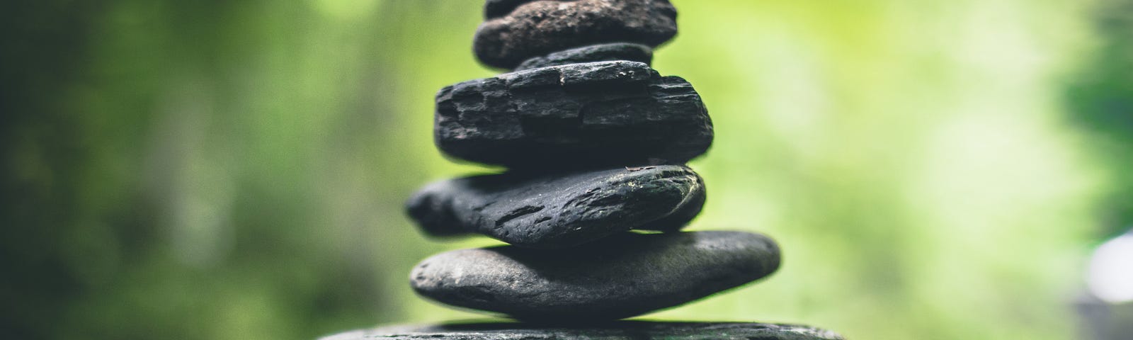 A beautifully photo’ed set of dark flat stones balanced from large to small in a tower placed on a rock surface in the open greenery in daylight.