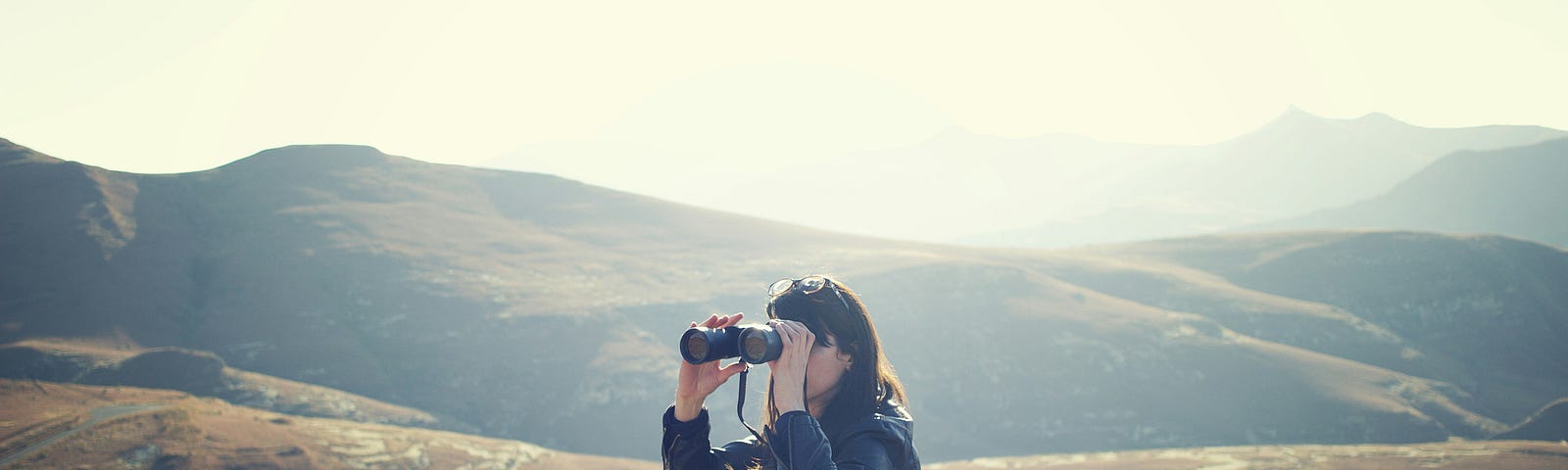 a woman with binoculars, sitting near a mountain hiking trail