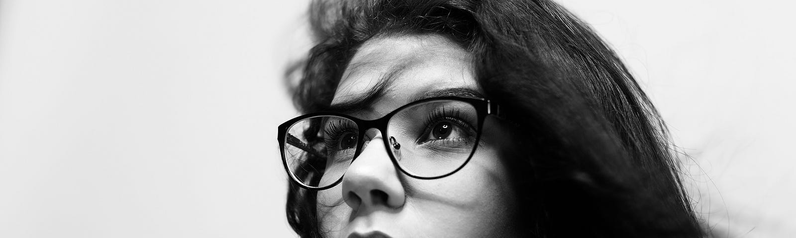 a black and white photo of a young girl’s face, hair loose, wearing glasses