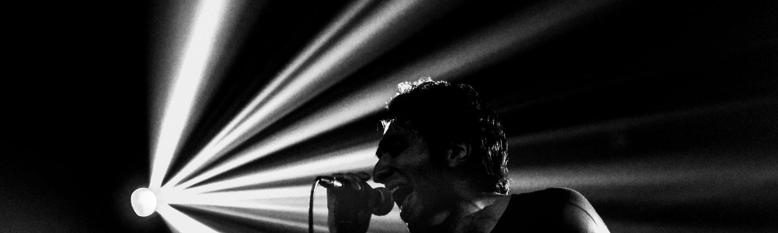 A rock singer back lit by streaks of white light screams into a microphone.