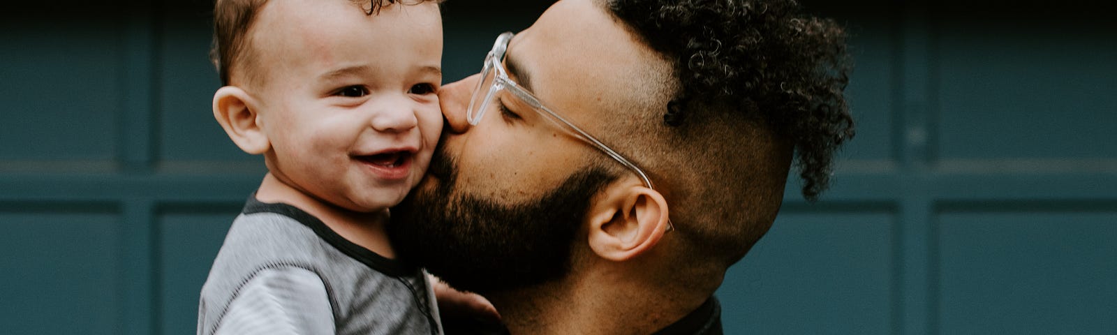 Father holding his smiling toddler son and kissing his cheek.