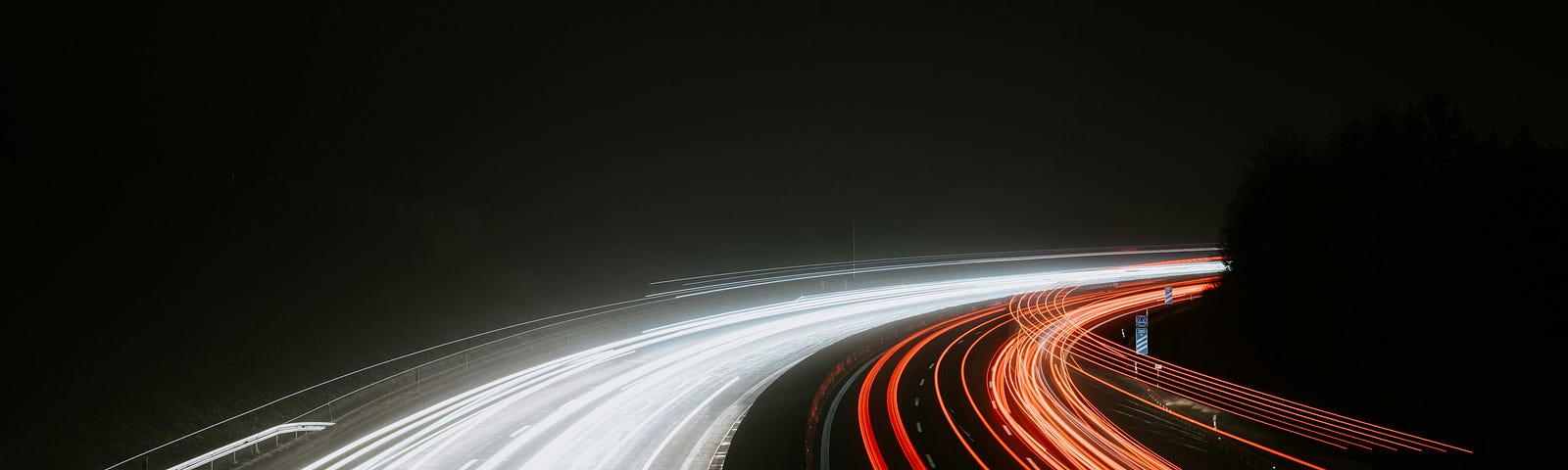 A long-exposure, night photo of a freeway showing the blur of many car lights moving around a bend.