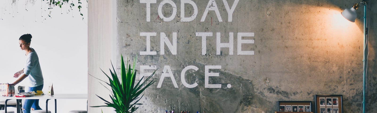 A modern office setting with the words Punch Today in the Face painted in white letters on the concrete wall