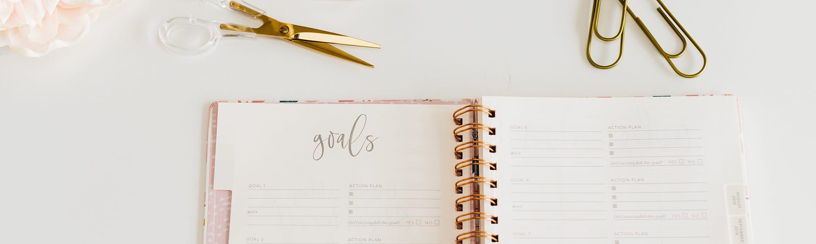 A pink journal for setting goals sits on a desk with other desk accessories.