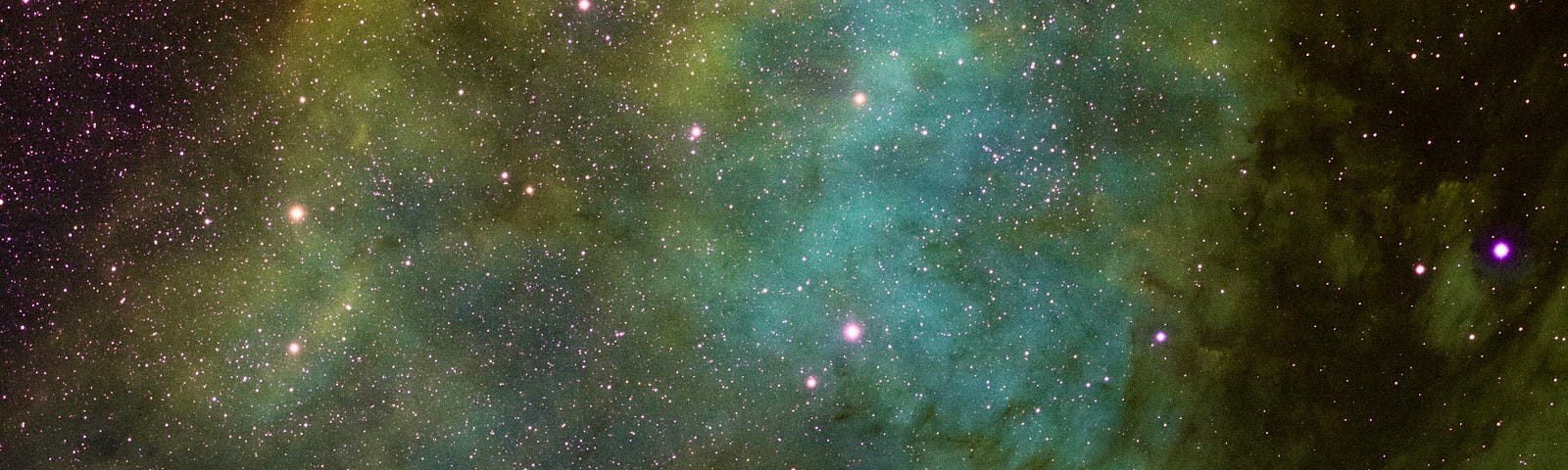 Image: a green-blue nebula, edged with yellow, blooming in deep space among multicoloured stars.